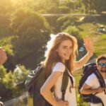 Group of happy friends with backpacks walking down hiking trail on sunny day in summertime